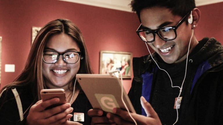 Two young people smile while holding smart devices
