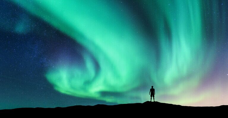 Aurora borealis and silhouette of standing man. Sky with stars and green polar lights.